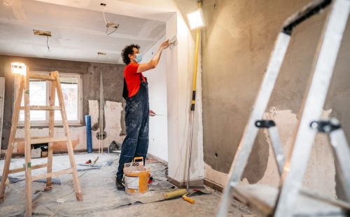 Construction worker plastering and smoothing concrete wall in room. Renovating apartment.