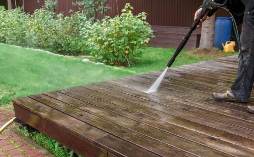 Man cleaning walls and floor with high pressure power washer. Washing terrace wood planks and cladding walls. High quality photo