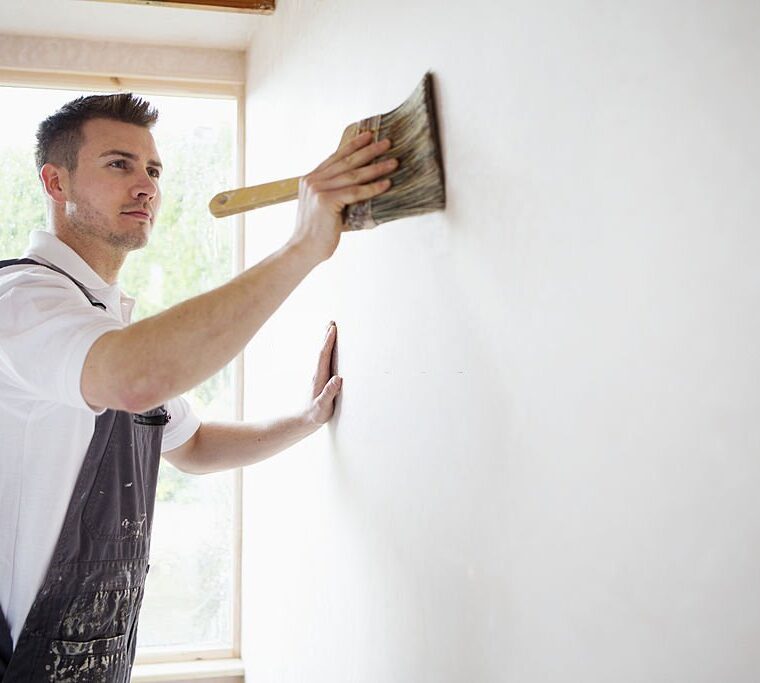 Young male decorator concentrating on his painting while watching the paintbrush.