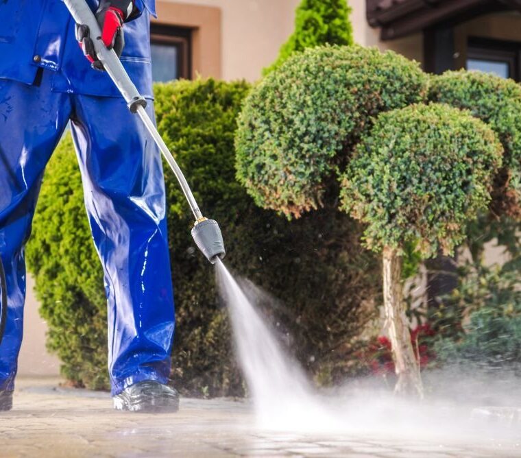 Caucasian Worker in His 30s with Pressure Washer Cleaning Residential Driveway. Garden and Home Surrounding Maintenance.