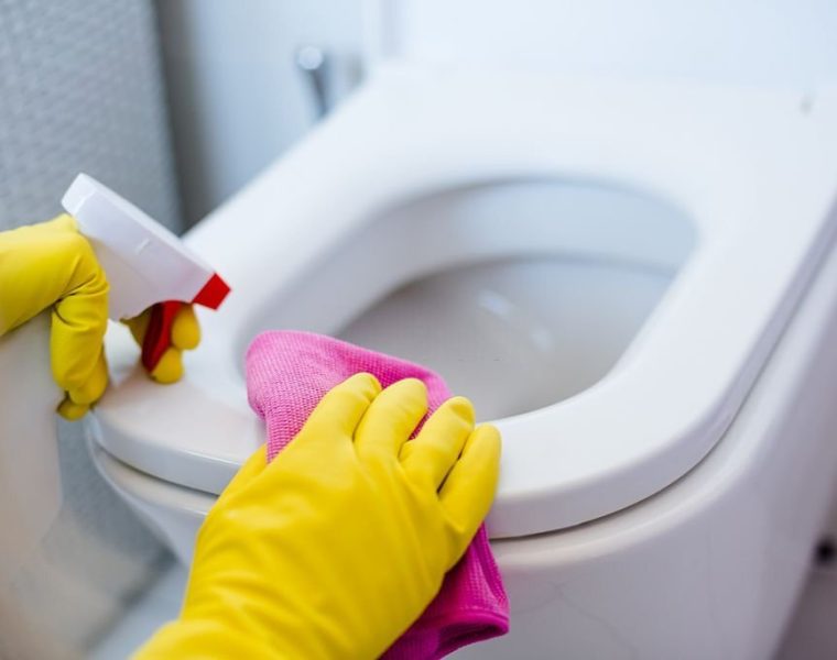 Woman in yellow rubber gloves cleaning toilet with pink cloth