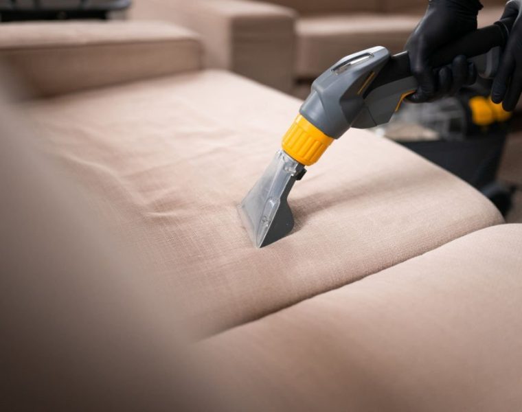 Sofa cleaning by a device. Close-up of housekeeper hand holding modern washing vacuum cleaner and cleaning dirty sofa with professionally detergent.